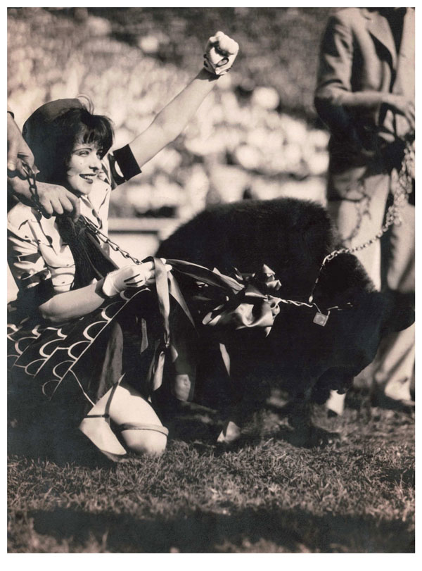 a woman holding the leash of a bear cub in one hand with her other hand raised in the air triumphantly.