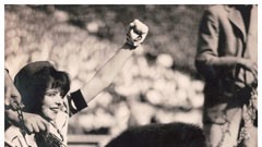 a cropped black and white image of a woman smiling with her clenched fist raised victoriously.